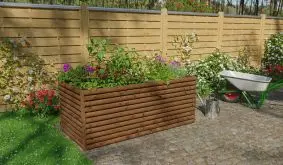 Bepflanztes Blumenhochbeet aus braunen Hölzern im Garten vor einem Zaun