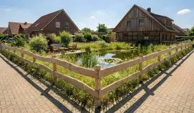 Rustikaler Bretterzaun Bonanza aus Lärchenholz mit unbesäumten Bohlen vor Fachwerkhaus im Garten.