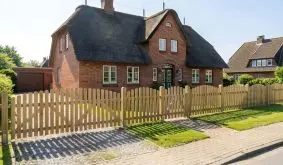 Gartenzaun mit senkrecht angeordneten Zaunlatten und Oberbogen inkl. Tor und Doppeltor vor Reetdachhaus in Norddeutschland.