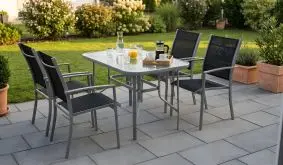 Garten Sitzgruppe Ravello mit grauem Stahlgestell, vier schwarzen Stapelsesseln und Glastisch auf Terrasse.