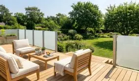 Glaszaun San Sebastian II aus satiniertem Mattglas, milchige Glasfelder an grauen Pfosten, auf Holzterrasse im Garten