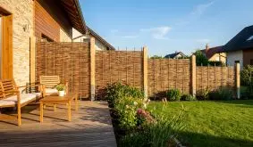 Haselnusszaun aus geflochtenen Ruten zwischen Holzpfosten, Sichtschutz an Terrasse und Rasen