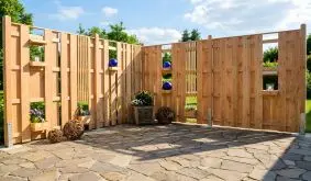 Holz Terrassenabtrennung aus hellem Holz mit integrierten Regalen und offenen Feldern auf gepflasterter Terrasse im Garten.