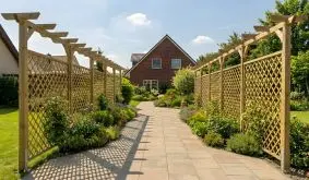 Beidseitig mit Holzpergolen und Rankgittern gesäumter Weg im Garten vor einem Wohnhaus.