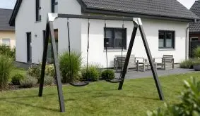 Schaukelgestell Luxus, schwarz grundiertes Holzgestell mit zwei Schaukelsitzen im Garten vor modernem Haus
