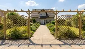Ranksystem Poel Holz-Rankgitter mit Hochbogen in einer Pergola, links und rechts am Gartenweg vor einem Haus