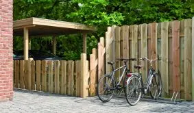 Sichtschutzzaun Frankfurt aus Holz mit senkrechten abgerundeten Latten, Zaun mit Schrägelement entlang des Weges zwischen Haus und Carport.