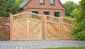 Dekorativer Holzzaun mit Gittermuster im Garten, geschwungene Form, umgeben von grünen Bodendecker-Pflanzen und Steinmauer.