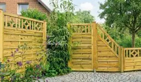 Dekorativer Holzsichtschutz als Terrassenabtrennung im Garten mit ornamentalen Elementen mit Nachbarhaus im Hintergrund.
