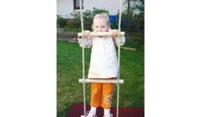 Strickleiter mit Holzsprossen im Garten montiert, Kind steht auf unterster Sprosse. Robuste Schaukelleiter für Kinder ab 3 Jahren.