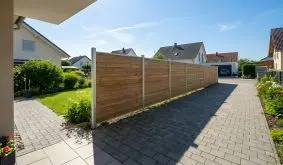 Thermo Holzzaun mit horizontalen Holzlamellen zwischen Aluminiumpfosten, montiert als Trennung zwischen Vorgarten und Einfahrt.
