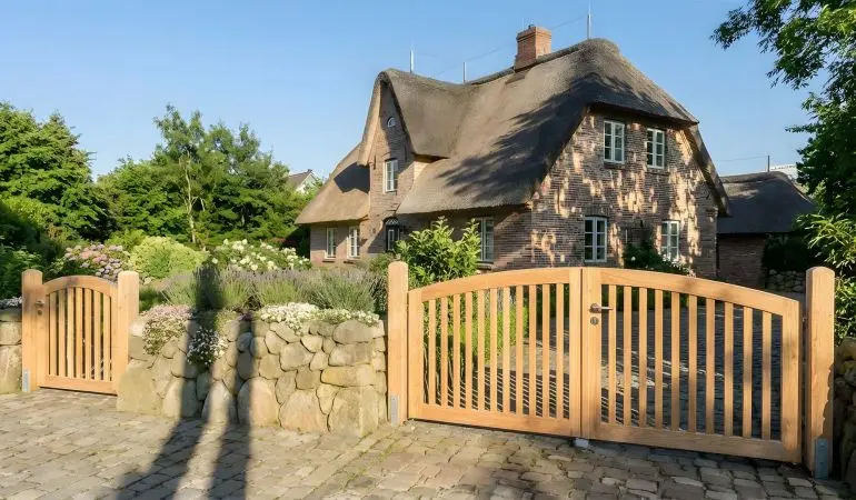 Stilvolles Gartentor und Doppeltor mit umlaufenden Rahmen und senkrechten Latte, montiert zwischen Friesenmauer vor Reetdachhaus.