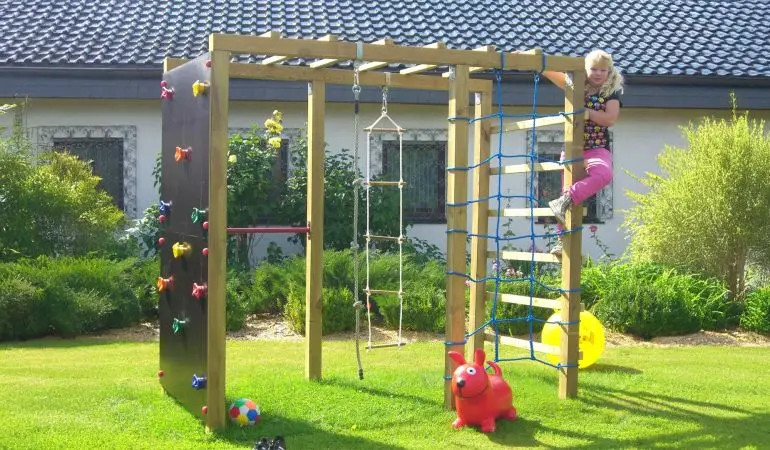 Kletterturm mit Strickleiter, Kletterwand, Reckstange und weiteren Klettermöglichkeiten im Garten vor einem Haus