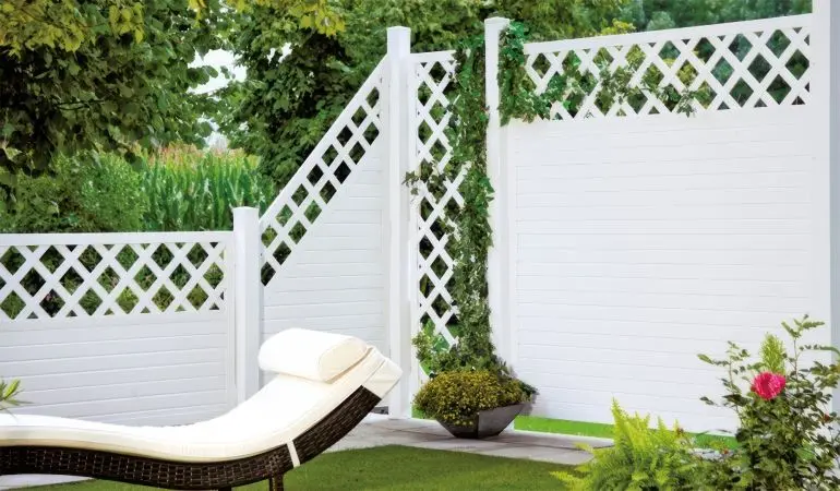 Moderner Sichtschutz aus weißem Kunststoff mit Gitteroptik im Garten, daneben eine Rattanliege und dekorative Pflanzen.