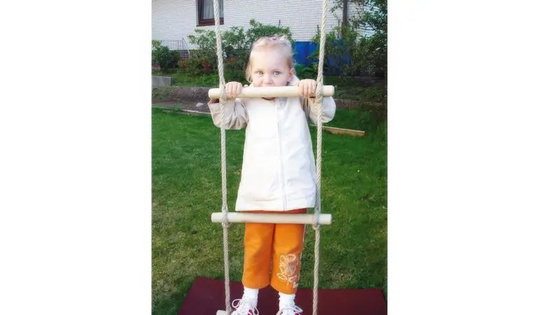 Strickleiter mit Holzsprossen im Garten montiert, Kind steht auf unterster Sprosse. Robuste Schaukelleiter für Kinder ab 3 Jahren.
