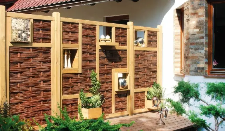 Moderner Sichtschutz aus Holz und Weide mit integrierten Deko-Nischen und Pflanzgefäßen auf einer Terrasse, rustikaler Gartenzaun.