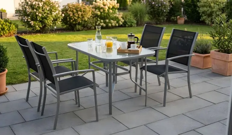 Garten Sitzgruppe Ravello mit grauem Stahlgestell, vier schwarzen Stapelsesseln und Glastisch auf Terrasse.
