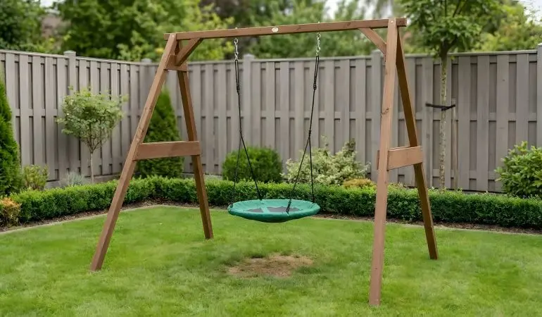 Nestschaukel mit Gestell aus braunem Holz mit grünem Rundsitz, aufgehängt im Garten auf Rasen