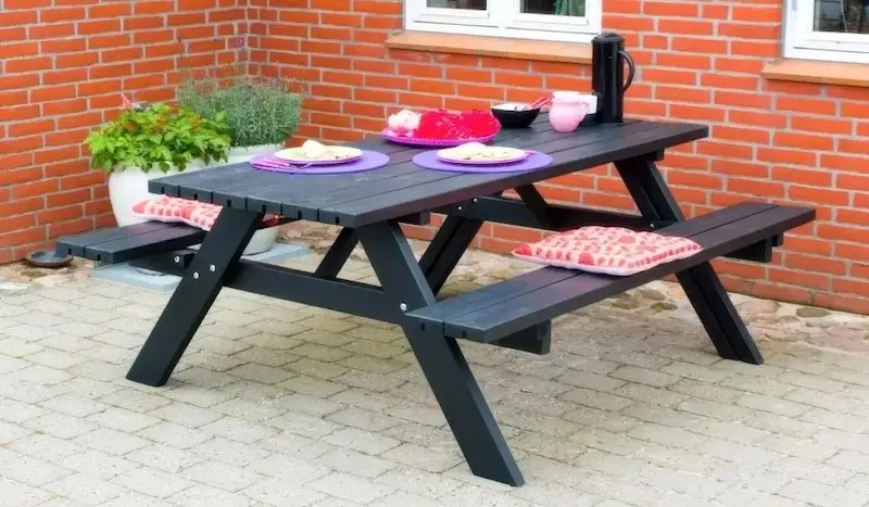 Picknicktische – die „All-in-one“-Lösung für den Außenbereich Schwarz grundierter Picknicktisch aus Holz auf gepflasterter Terrasse
