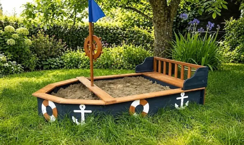 Sandkasten in Bootsform aus Holz Holz-Sandkasten in Bootsform mit Sitzbank, Steuerrad und Fahne im Garten