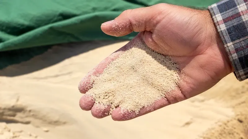 Feinkörniger Spielsand für den Sandkasten Männerhand mit feinkörnigem Spielsand über einem Sandkasten