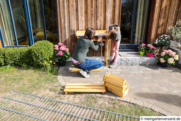 Frau und Mädchen bauen Pflanztisch auf